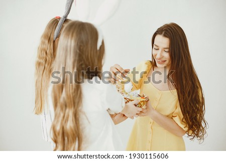 Girls with a basket of eggs. Happy mom in a yellow dress. Long hair in girls.