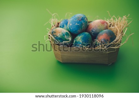 Multicolored Easter eggs lie in a basket on a green background, close-up.
