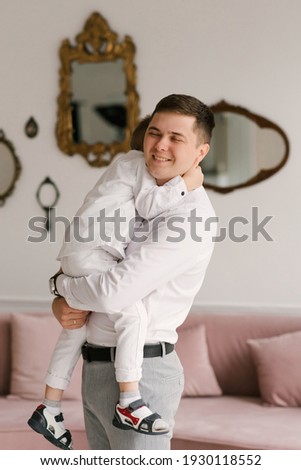 Beautiful young dad and son cuddle and play in smart clothes at home