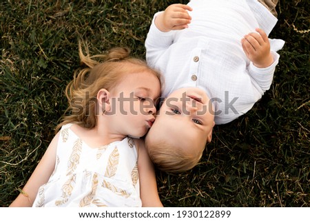 Cute little girl kissing her brother on his forehead outside on a sunny day