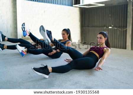 Strong beautiful woman doing flutter kicks in the gym. Caucasian young women in sporty clothing training with a cardio workout and HIIT routine Royalty-Free Stock Photo #1930135568