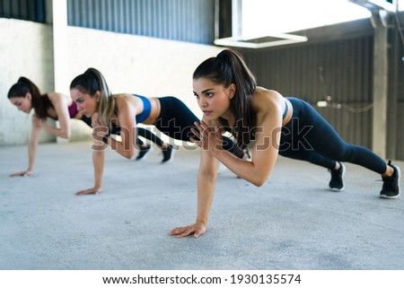 Group of women doing shoulder taps during a high-intensity interval training at the gym. Three fit caucasian women working out with a cardio routine indoors  Royalty-Free Stock Photo #1930135574