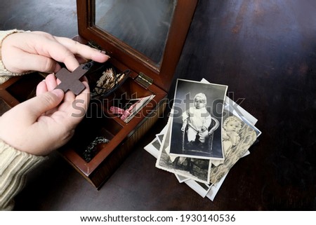 female hands sorting dear to heart memorabilia in old wooden box, stack of retro photographs, wooden cross, vintage photographs of 1960, concept of family tree, genealogy, childhood memories Royalty-Free Stock Photo #1930140536