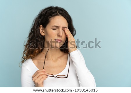 Sleepy young caucasian woman holding glasses rubbing eyes, feels tired after working on computer, isolated on blue background. Exhausted office employee suffering from ocular diseases, eye strain.  Royalty-Free Stock Photo #1930145015