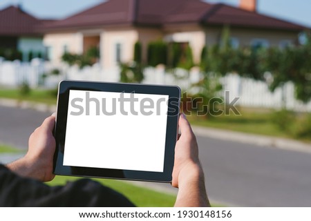 A tablet in the hands of a man, against the backdrop of a house