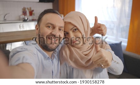 Muslim husband and wife taking selfie  happily 'okay' sign with thumbs up. Frontal camera wiev.