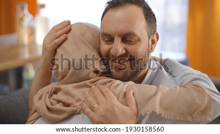 The bearded young man who hugs his wearing a headscarf Muslim wife and consoles her. Happy family portrait.