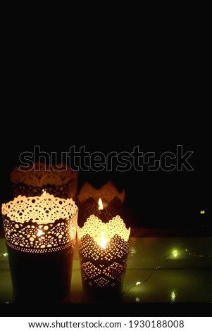 Two candle holders with lit candles in the dark. Selective focus, bokeh fairy lights.