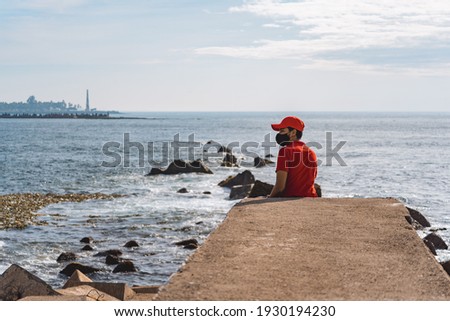 Man wearing surgical mask to prevent covid 19 on the shore watching the ocean