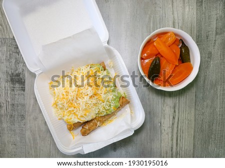 Five rolled tacos topped with guacamole, sour cream and cheese in a take out container and a side of hot carrots.