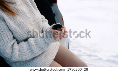 Close up, young woman leaning on the car and driniking hot beverage from the thermal bottle . High quality photo