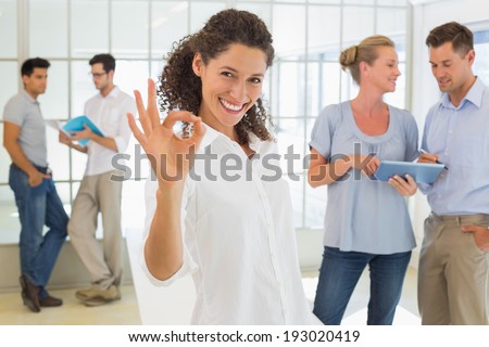 Casual businesswoman giving ok sign to camera in the office