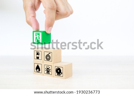 Close-up hand choose wooden toy blocks stacked with door exit sing icon with fire extinguisher and fire protection symbol for safety prevent and protect accident of emergency and rescue.