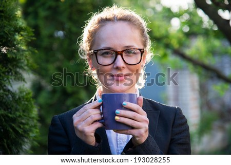 Girl in glasses holding a blue cup in hands. Girl looks in the picture.
