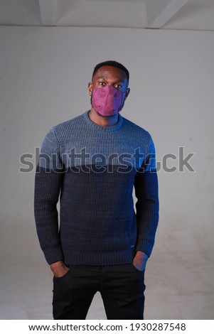 Three quarter length portrait of black handsome Man wearing fabric hygienic protective cloth face mask against coronavirus, studio shot isolated grey background, COVID-19 medical concept