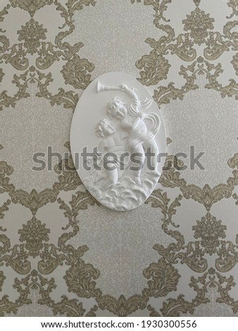 plaster round picture with two angels on wallpaper with a pattern