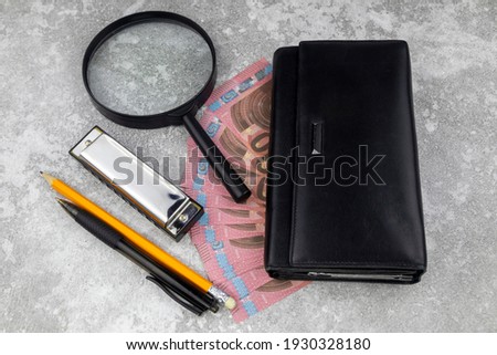 Financial, business success or analysis concept with 10 Euro bills fanned below a purse with magnifying glass, pen and pencil on a decorative wood background in a high angle view