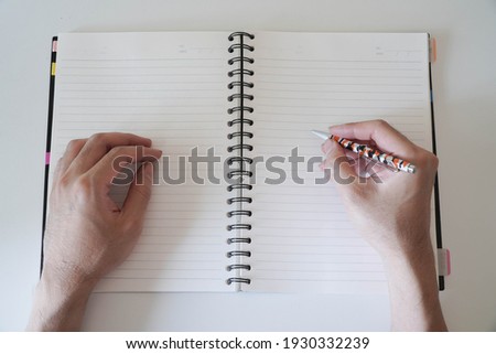 man's hand written in a spiral notepad placed on a wooden table with items.studying, signing, education, school, institute, university, office and working concept