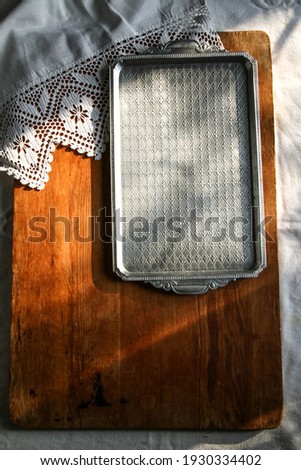 old wooden board on a white linen tablecloth and a metal rectangular tray lace towel sunny natural light, shade. kitchen table top view. Beautiful retro, rustic background, free space.