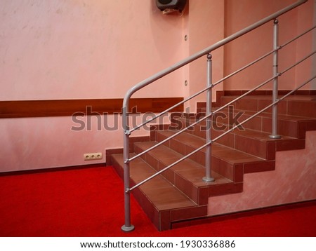 Staircase with shiny metal railings indoors. Red carpet and light ceramic tiles. Business office center indoor stairs side view. Austere interior with a place for copyspace. Corridor way lift ladder.
