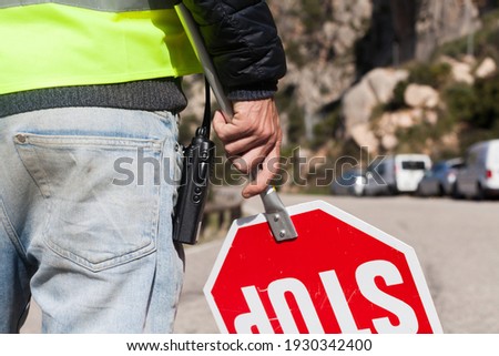 A road worker with a walkie talkie and a reflective vest while holding a stop sign on a mountain road in Majorca