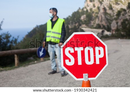 Road maintenance worker during the coronavirus pandemic, on a road with a stop sign and reflective vest