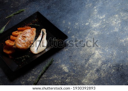 Grilled chicken steak with spices and baked potatoes on a black plate on a dark textured background with copy space.
