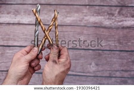 Metal drill bits. Dirty from work, men's hands hold drills on metal. On a wooden background.