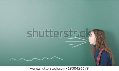 Pre-adolescent girl blowing. Portrait photo on school board background. High resolution photo. Full depth of field.