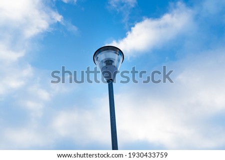 Beautiful transparent outdoor electricity lamp with background of blue cloudy sky, highlighted by the sun 