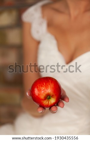 Red juicy apple in the hands of the bride in a wedding dress, a narrow area of sharpness, the bride against the background of a brick wall is out of focus. High quality photo