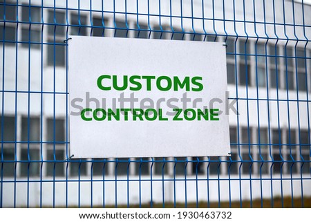 Customs control zone sign with green letters on metal fence, warning about entering special area. Security checkpoint of logistics complex, vehicle inspection point. Border symbol.