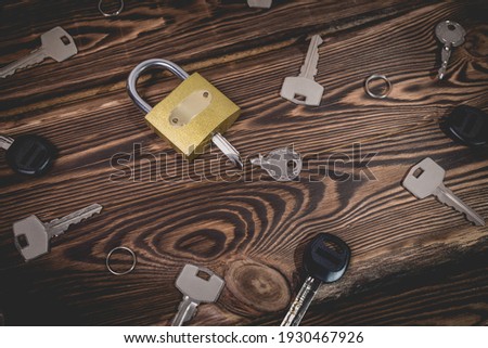 Studio photo of a lock with a broken key in it on a wooden background. Lots of other new keys around the lock. Photo in the old style with vignetting.