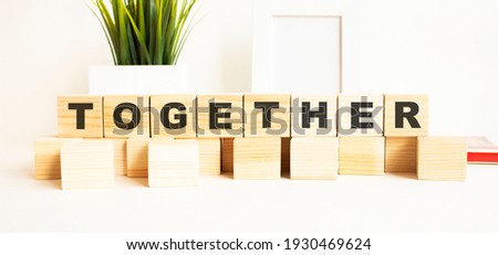 Wooden cubes with letters on a white table. The word is TOGETHER. White background with photo frame, house plant.
