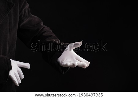 Hand gestures. Present something, the show begins. Showman or magician illusionist in white gloves on a black background.