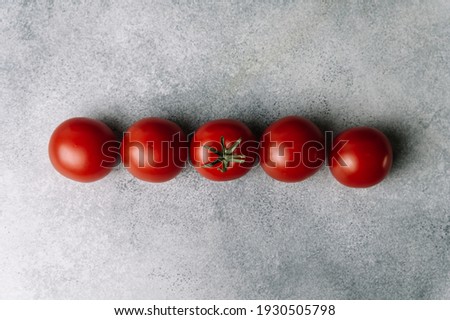 Line of red tomatoes on gray background in top view. Organic healthy food. Raw tomatoes. Fresh vegetables