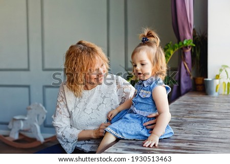 A loving mother plays with her child. Mother and daughter sit on the wooden floor near a large window.