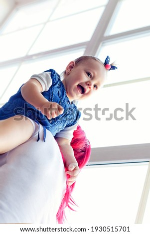 A loving mother plays with her child. A mother holds her daughter in her arms near a large window.