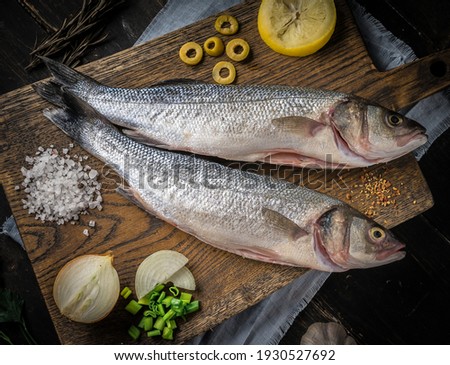Fresh raw seabass fish on cutting board. Culinary seafood background with ingredients for cooking. Top view