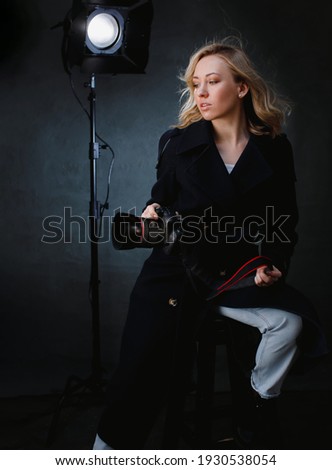 Female photographer journalist with professional camera taking photo in photo studiostudio lights. Girl making movie operator is on the background lighting. 