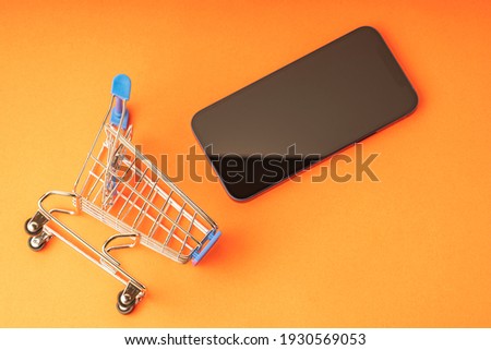 An empty shopping cart and a modern smartphone on a red scarlet background. Shopping, online shopping concept, copy space, top view, orange tinting