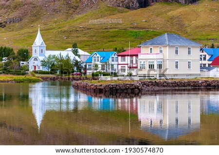 Cityscape view of the town of Seyðisfjörður (Seydisfjordur), Iceland and its reflection on the water of sea fjord. A light sign welcomes people arriving by ferry.