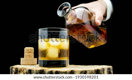 Pour whiskey into a glass with ice on a rustic on a black background. Whiskey in a clear glass.
