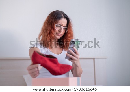 The woman unpacks the delivered shoes. A dissatisfied girl leaves a review about the order in the application on a smartphone