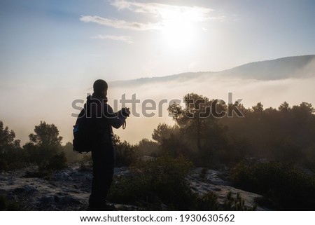 Photographer taking landscape pictures in a forest and a mountain in the morning on a cloudy and foggy day