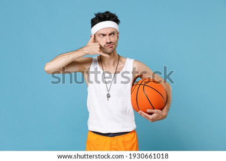 Excited fun young man basketball player with thin skinny body sportsman in headband shirt shorts whistle hold basketball ball posing isolated on blue background. Workout gym sport motivation concept.