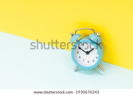 blue alarm clock over yellow background. studio shot. time concept. template for design.