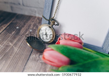 blank blue photo frame with vintage round clock and tulips on brick wall background