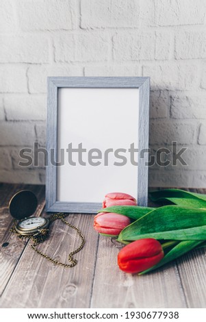 blank blue photo frame with vintage round clock and tulips on brick wall background