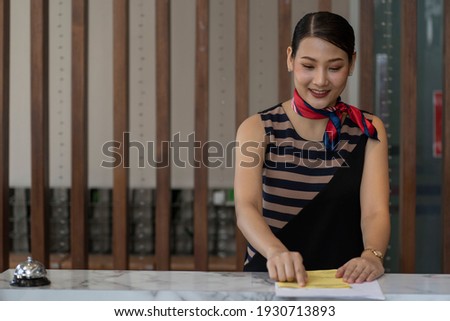  receptionist at counter in hotel wearing medical masks as precaution against virus. Young couple on a business trip doing check-in at the hotel